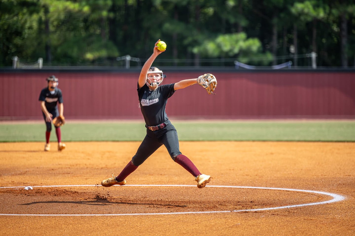 Hillgrove softball pitcher at full extension in her delivery, ball in hand, an infielder set behind her.